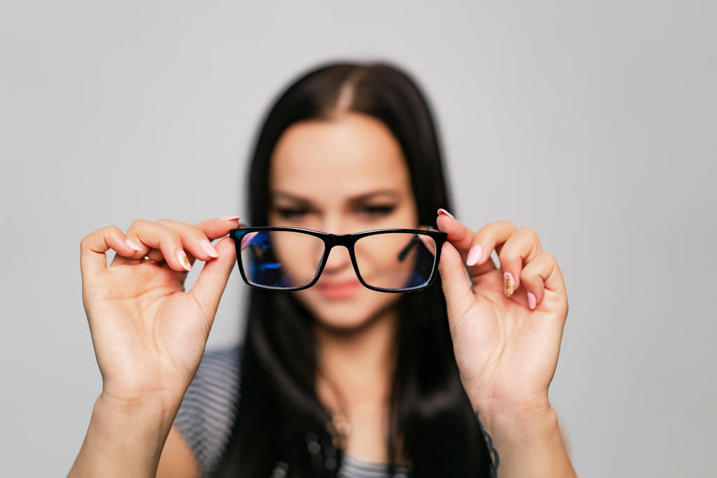 Die stylische Brille mit schwarzem Rand und innen transparenten Gläsern liegt in weiblicher Hand auf weißem Hintergrund. Nahaufnahme - Foto, Bild