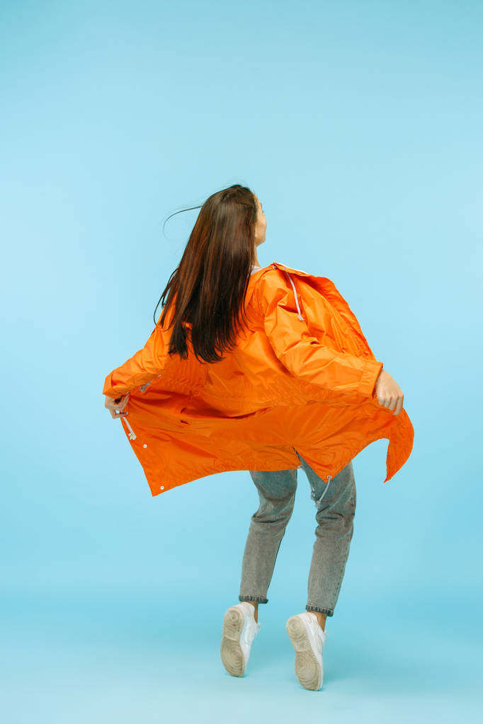 Η νεαρή κοπέλα ποζάρει στο studio στο μπουφάν που απομονώνονται σε μπλε - Φωτογραφία, εικόνα