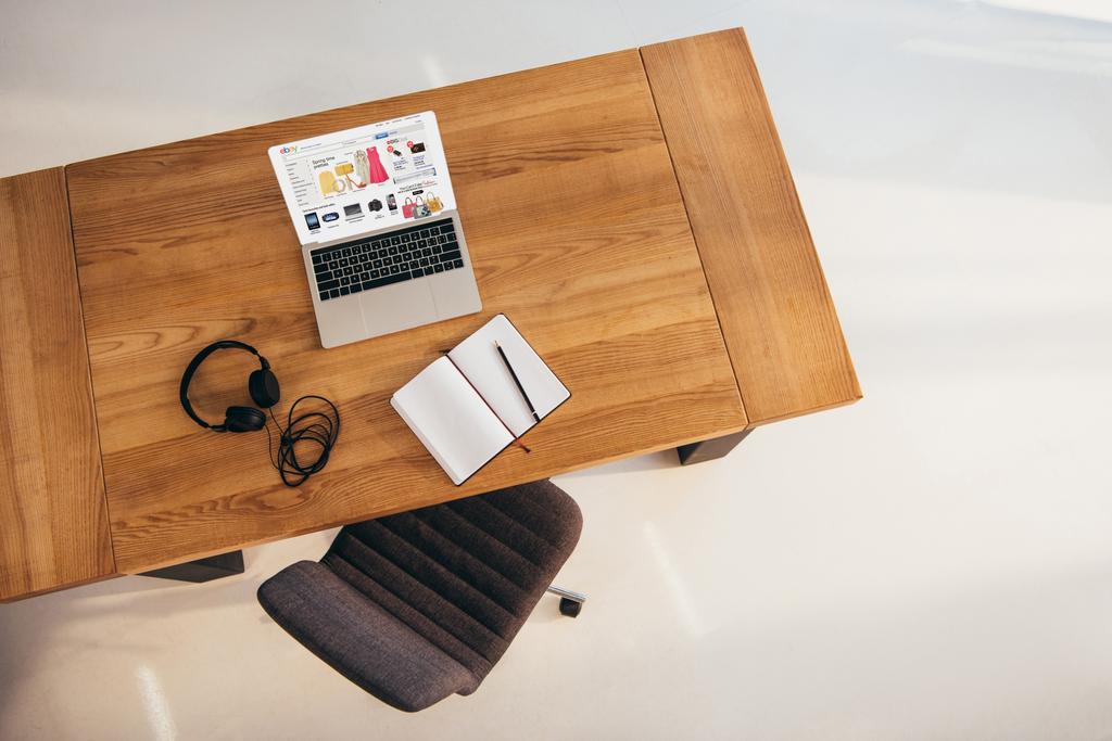 Widok z góry laptopa z witryny ebay, słuchawki i notebook na drewnianym stole z krzesłem biurowym w pobliżu przez - Zdjęcie, obraz