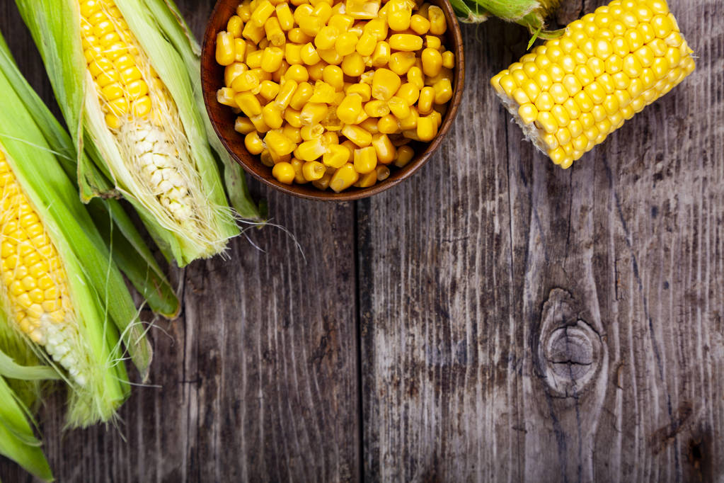 Ripe yellow corn and canned corn in a wooden bowl on a wooden table. Yellow ripe corn, top view - Photo, Image