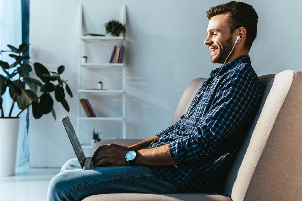Zijaanzicht van glimlachende man in oortelefoons die deelnemen aan de webinar thuis - Foto, afbeelding