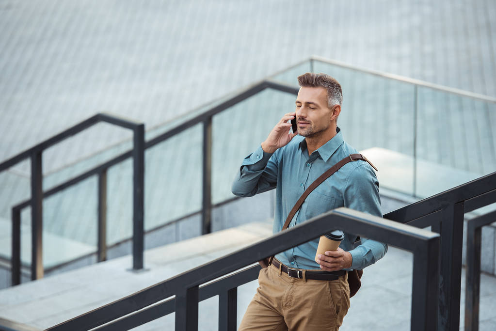 smartphone ile konuşmak ve kağıt bardak merdivenlerde dururken tutan orta yaşlı işadamı yüksek açılı görünüş - Fotoğraf, Görsel