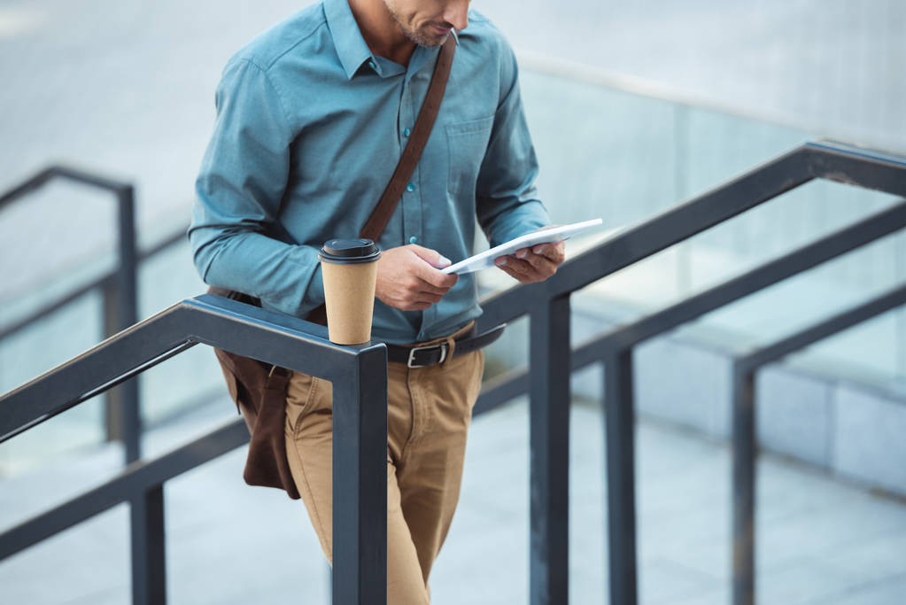 обрізаний знімок людини за допомогою цифрового планшета, стоячи на сходах з кавою, щоб піти на перила
 - Фото, зображення