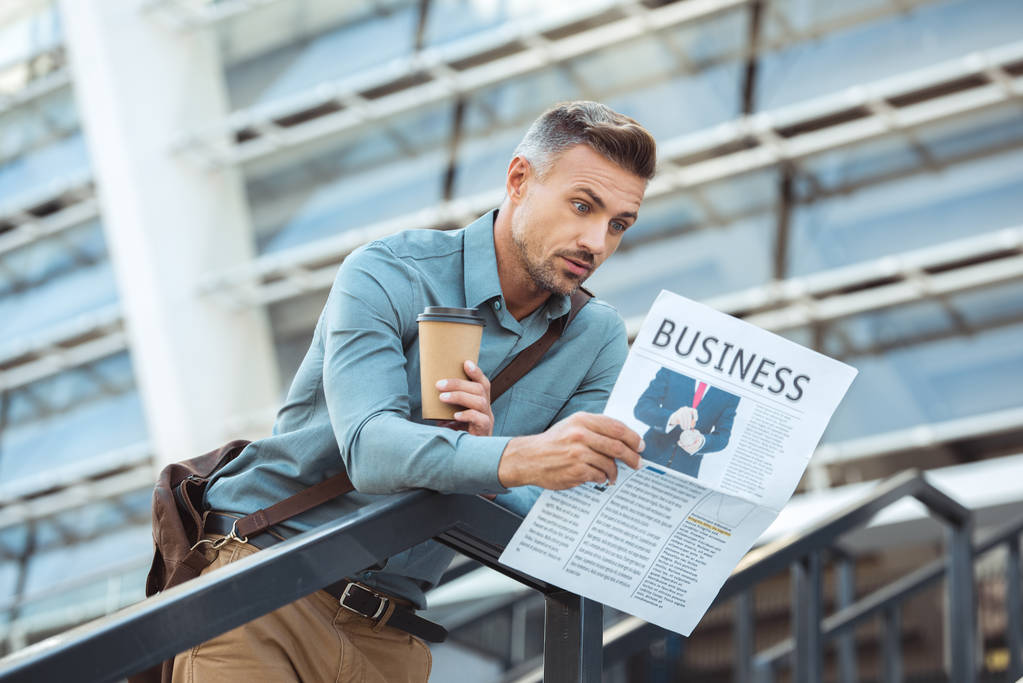 wstrząśnięty bliskiego wieku człowiek trzyma kawę na wynos i czytanie gazety biznes  - Zdjęcie, obraz