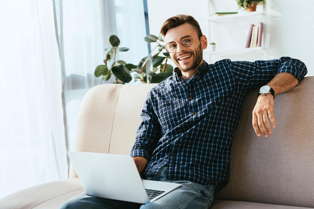 portret uśmiechnięty człowiek w okularach z laptopa siedząc na kanapie w domu - Zdjęcie, obraz
