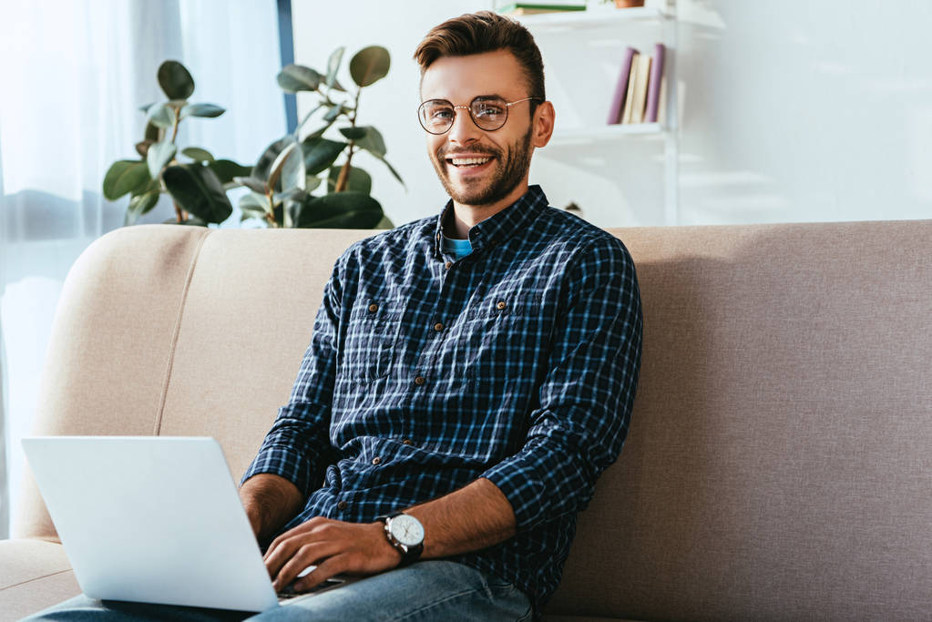 πορτρέτο της χαμογελαστός άνθρωπος σε γυαλιά με laptop κάθεται στον καναπέ στο σπίτι - Φωτογραφία, εικόνα