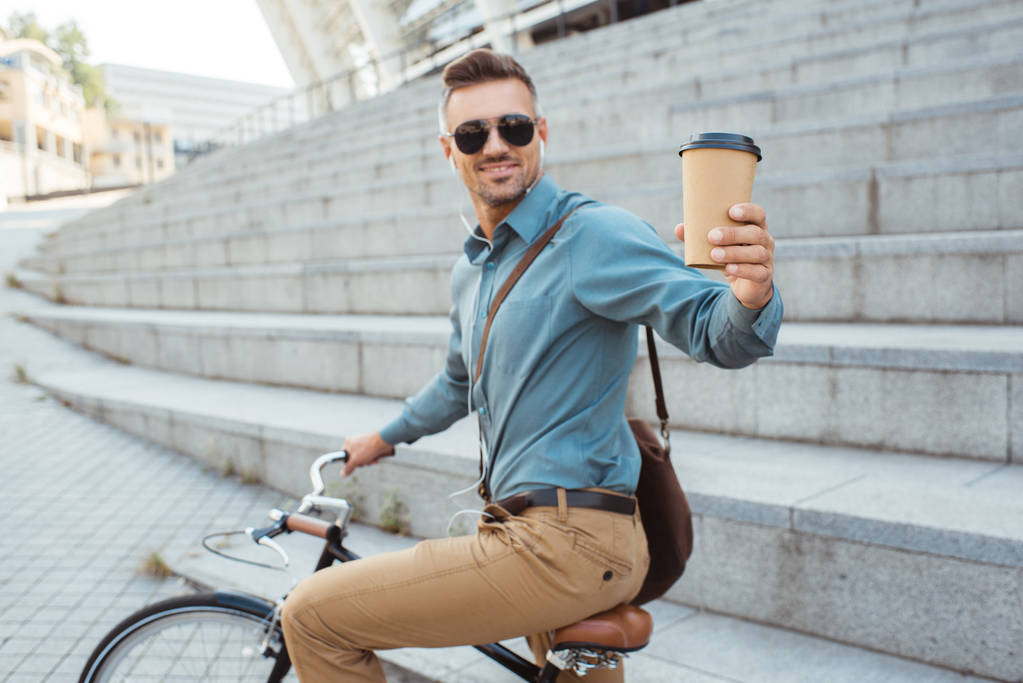 красивый улыбчивый мужчина, держащий кофе, чтобы покататься на велосипеде по улице
 - Фото, изображение