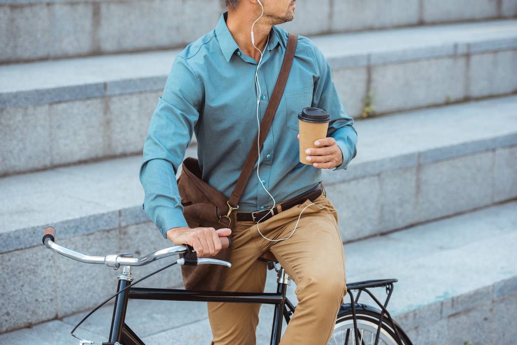 Kağıt bardak tutan ve bisiklet üzerinde oturan kulaklıklar insanın kırpılmış atış - Fotoğraf, Görsel