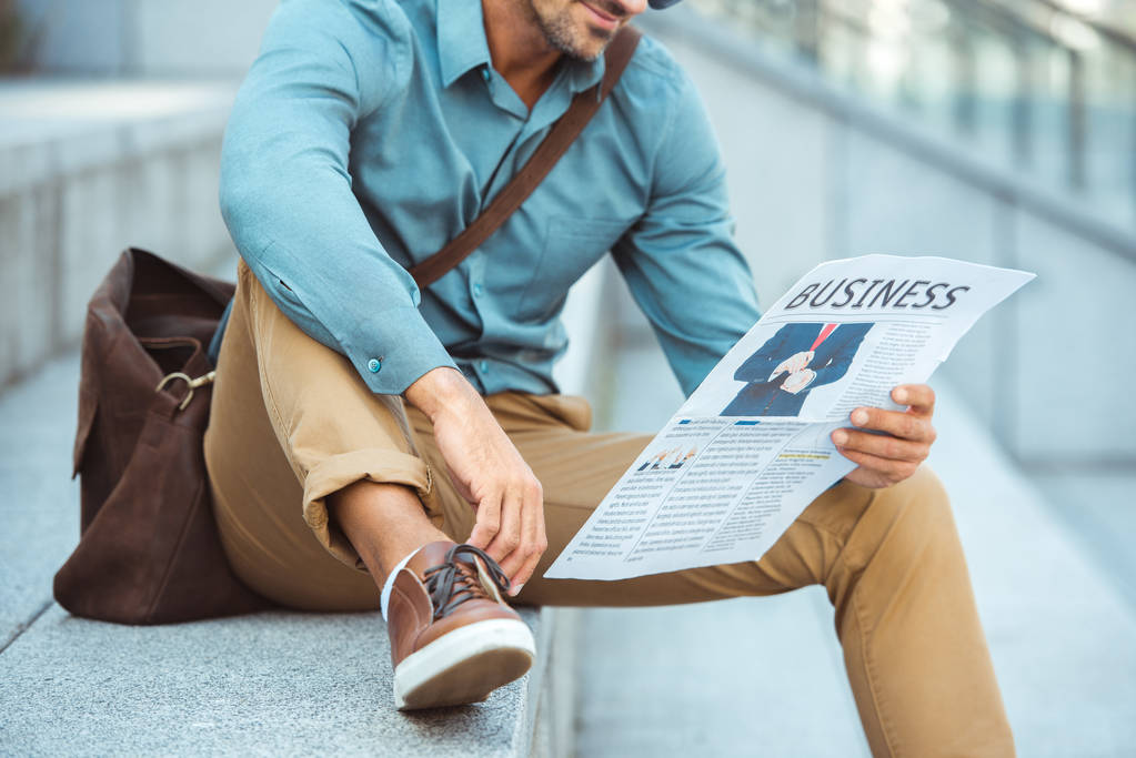 обрізаний знімок людини, що сидить на сходах і читає ділову газету
 - Фото, зображення