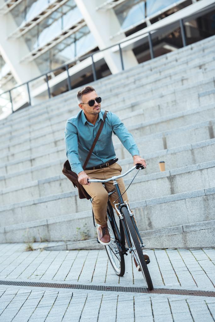 κομψό μέσης ηλικίας άνδρα σε γυαλιά ηλίου ιππασία ποδήλατο στο δρόμο  - Φωτογραφία, εικόνα