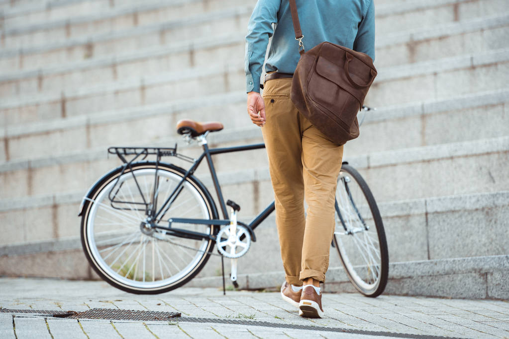 задний вид человека с кожаной сумкой, идущего на велосипед, припаркованный на улице
  - Фото, изображение