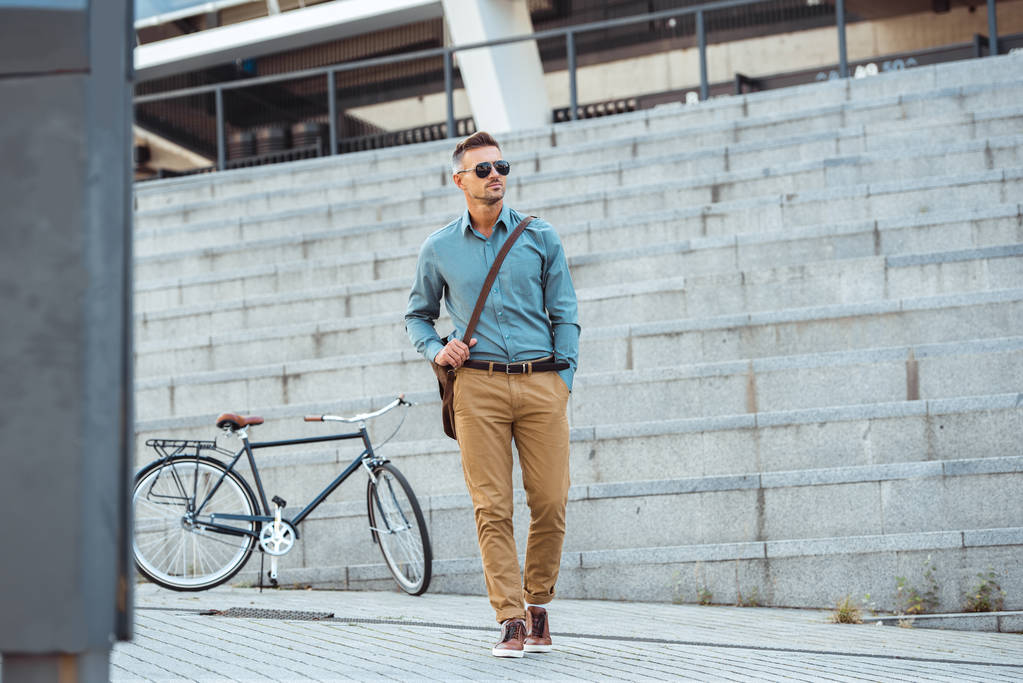 guapo hombre de negocios de mediana edad en gafas de sol caminando por la calle, bicicleta en el fondo
 - Foto, imagen