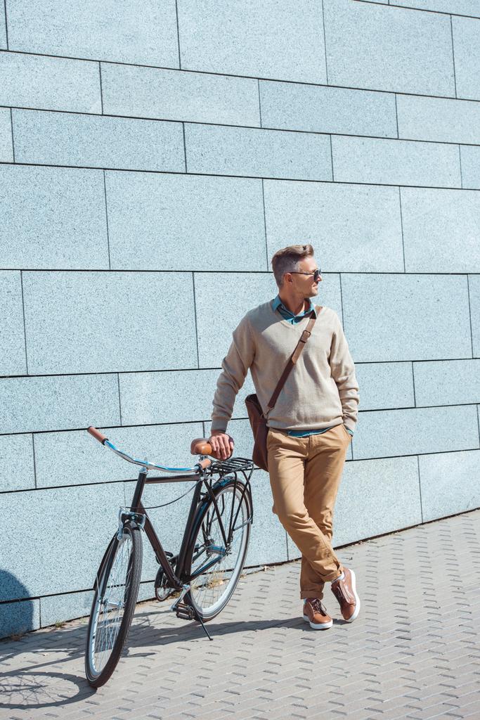 стильный мужчина средних лет в солнцезащитных очках, склоняющийся на велосипеде и смотрящий на улицу
  - Фото, изображение