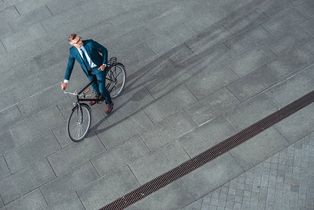 высокий угол обзора красивого бизнесмена в костюме и очках, сидящего на велосипеде и смотрящего в сторону
  - Фото, изображение
