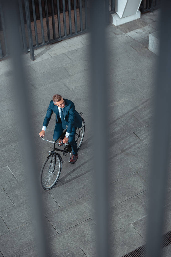 high angle view of businessman in formal wear riding bicycle and looking away on street  - Photo, Image