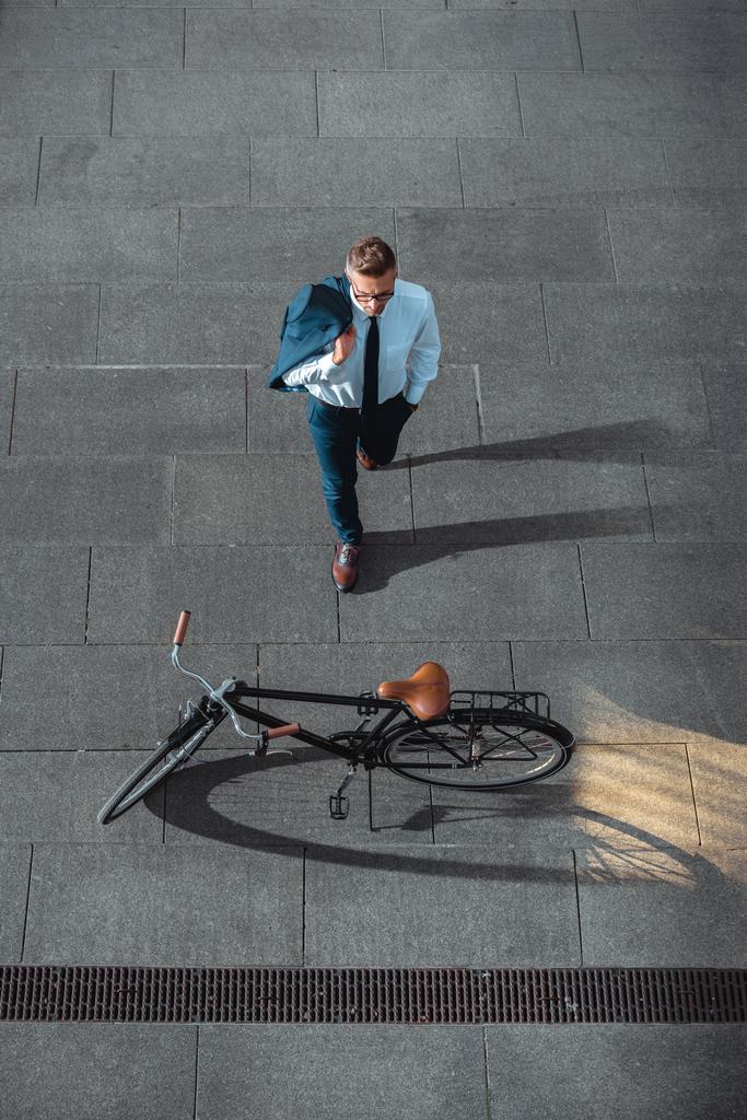 visão de alto ângulo de empresário segurando jaqueta terno e olhando para a bicicleta na rua
   - Foto, Imagem
