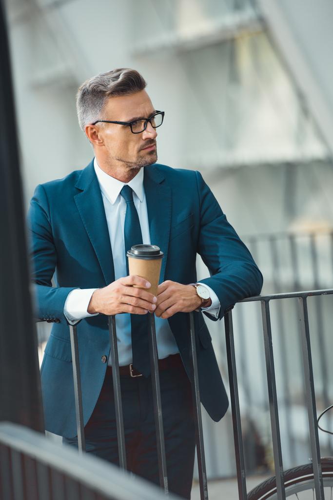 serious middle aged businessman in eyeglasses holding paper cup and looking away - Photo, Image