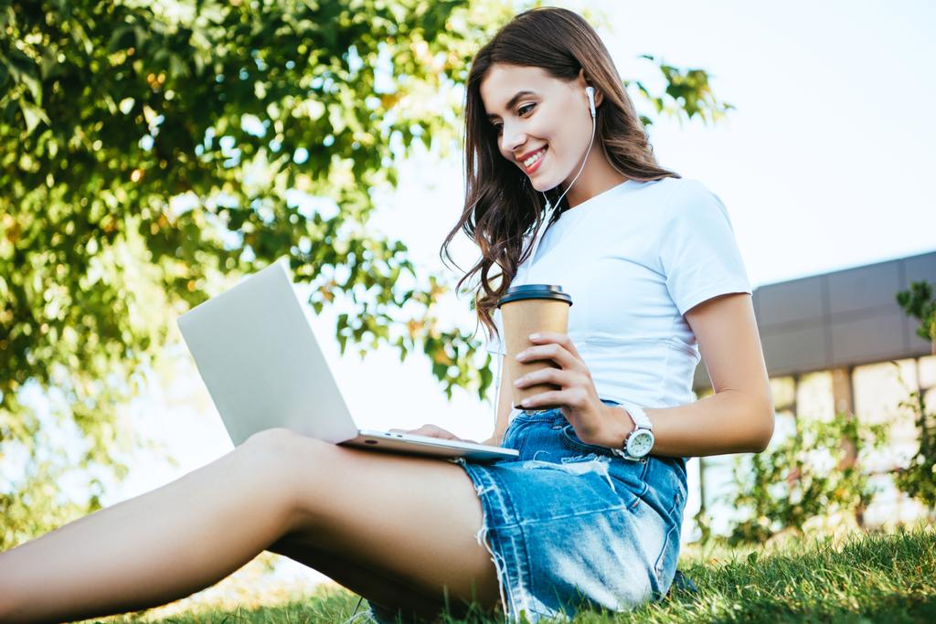 Seitenansicht des lächelnden schönen Mädchens, das an einem Webinar mit Laptop im Park teilnimmt - Foto, Bild