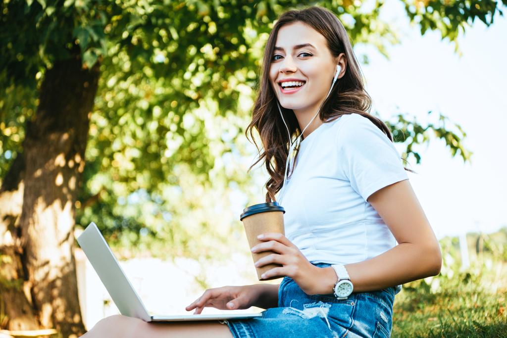 χαμογελώντας όμορφη κοπέλα λαμβάνοντας μέρος στο webinar με το laptop στο πάρκο, βλέπουν τα φωτογραφικών μηχανών - Φωτογραφία, εικόνα