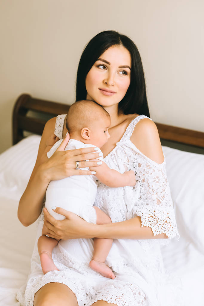 mutlu genç anne yatakta evde oturan küçük bebeği ile - Fotoğraf, Görsel