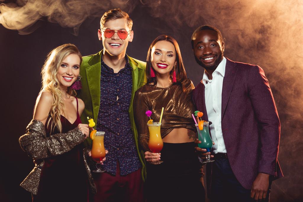 sonrientes amigos multiculturales sosteniendo cócteles de alcohol en la fiesta
 - Foto, Imagen