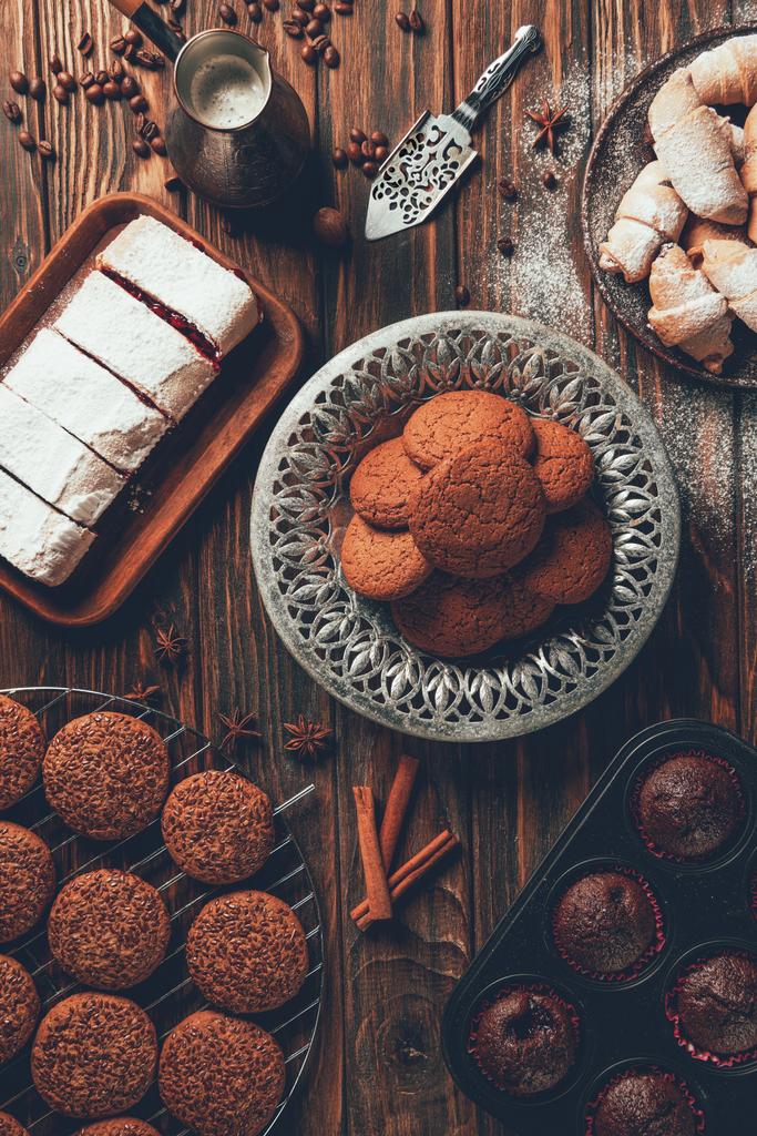 Blick von oben auf leckere gebackene Süßigkeiten auf Tellern und Blechen in der Bäckerei - Foto, Bild