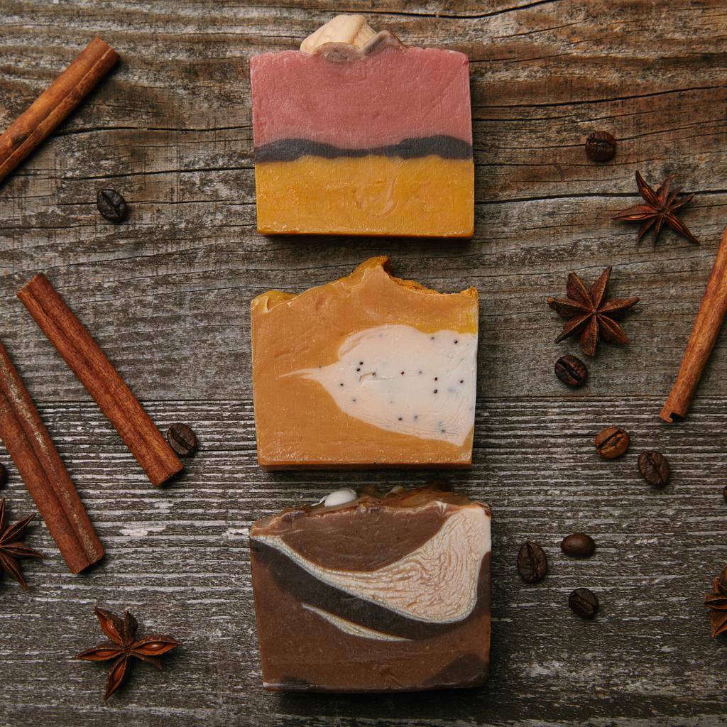 Draufsicht auf verschiedene handgefertigte Seifenstücke mit Gewürzen auf rustikaler Holzplatte - Foto, Bild