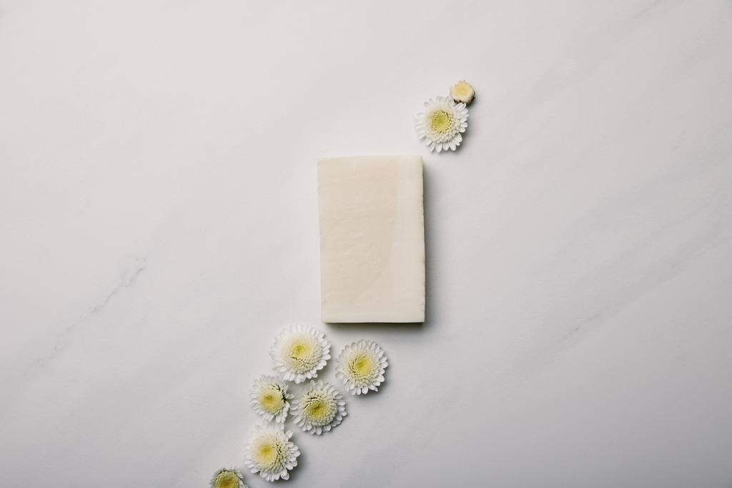 vista superior de la pieza de jabón blanco con margaritas en la superficie de mármol blanco
 - Foto, imagen
