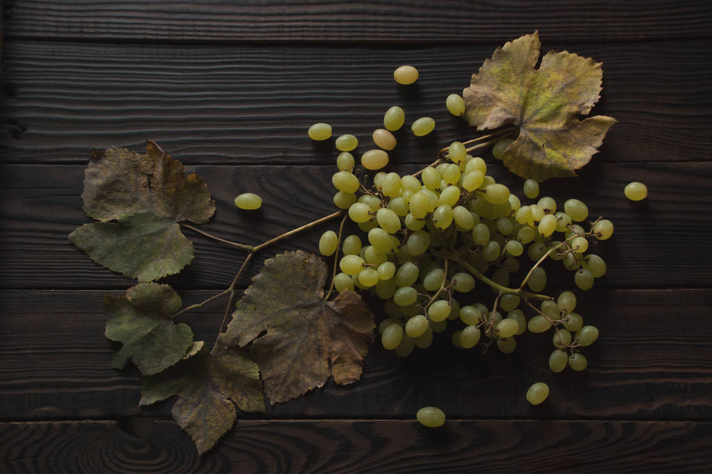 Bunch of white grapes, dry leaves on the dark wooden surface. Top view - Photo, Image