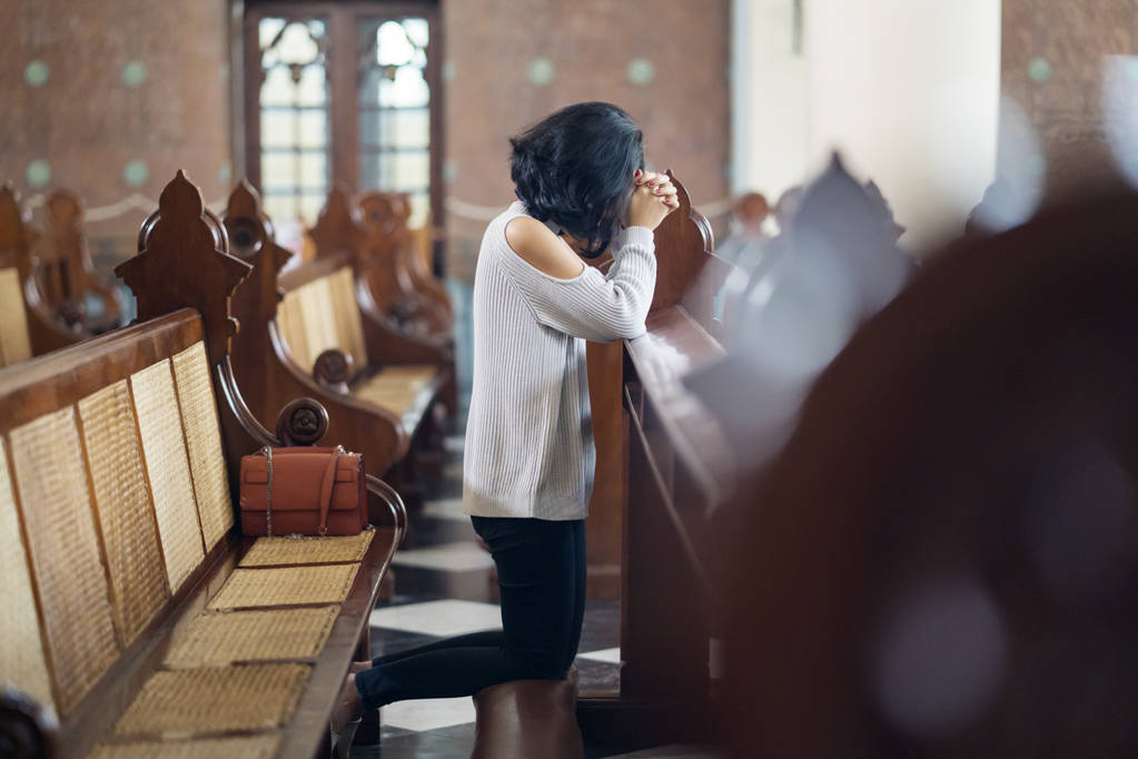 Vista lateral de una joven sentada con las manos apretadas en la iglesia mientras rezaba a DIOS
 - Foto, imagen