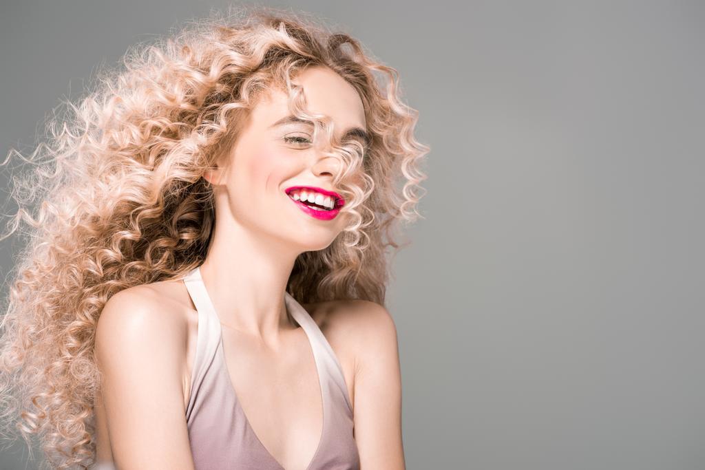 πορτρέτο του happy νεαρή γυναίκα με μακριά σγουρά μαλλιά γελώντας απομονώνονται σε γκρι - Φωτογραφία, εικόνα