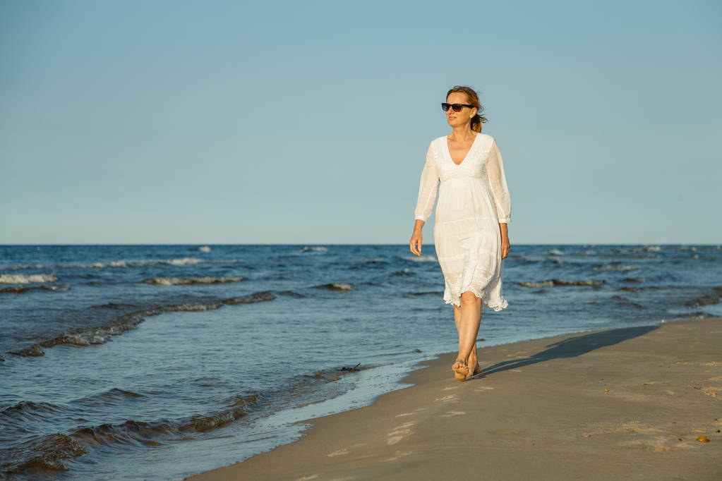 Femme adulte en robe blanche marchant au bord de la mer
 - Photo, image