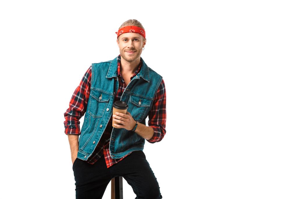 smiling man in headband and denim vest sitting on chair with coffee cup isolated on white - Photo, Image