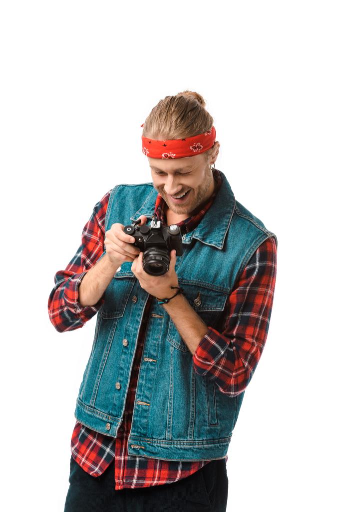 Lächelnder männlicher Hipster-Fotograf in Jeansweste und kariertem Hemd, der isoliert auf den weißen Kamerabildschirm blickt - Foto, Bild