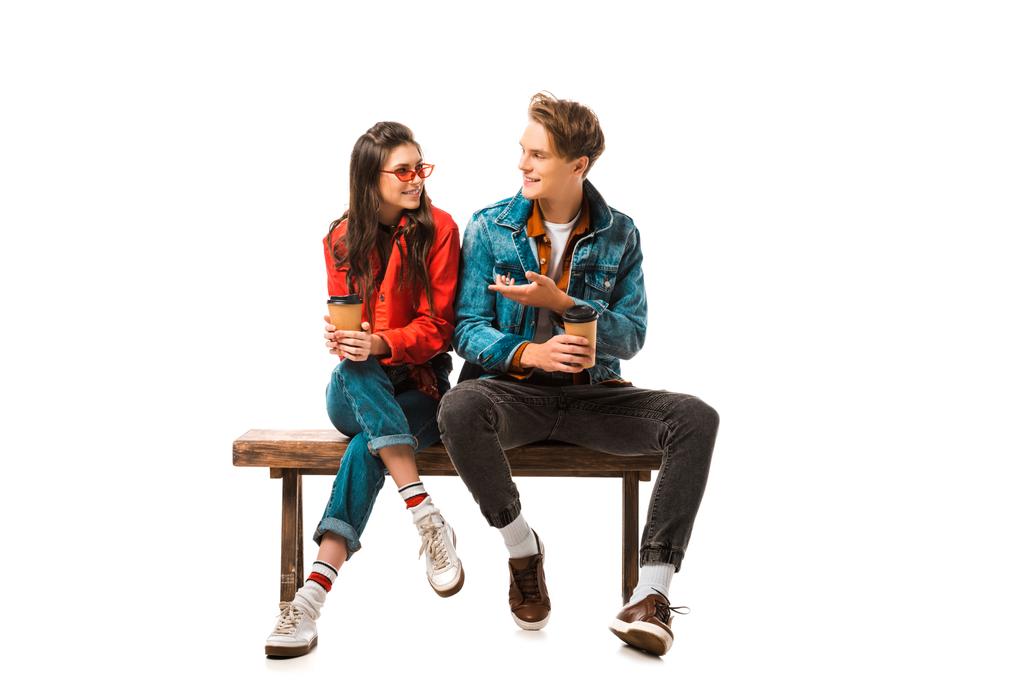 male hipster with paper cup of coffee pointing to girlfriend sitting on bench isolated on white - Photo, Image