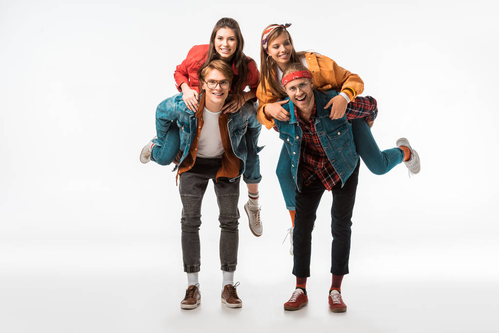 cheerful stylish hipsters doing piggyback ride to their smiling girlfriends isolated on white - Photo, Image