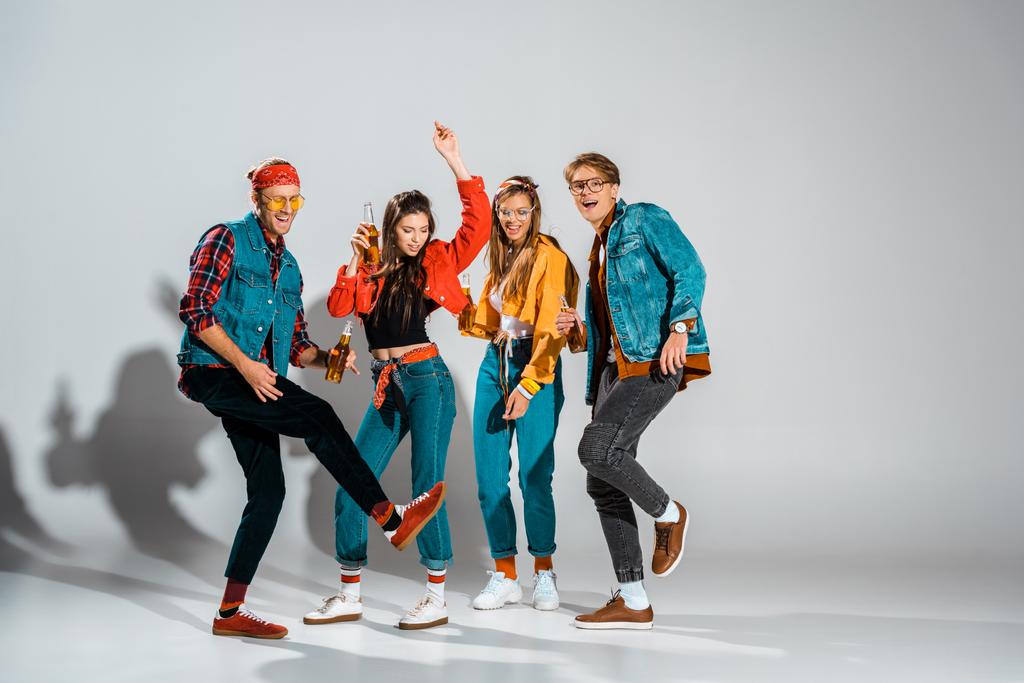 cheerful stylish hipsters with beer bottles dancing together on grey - Photo, Image