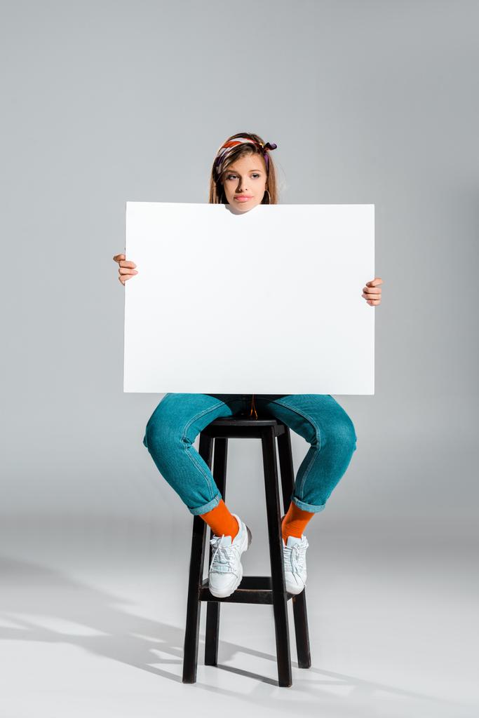atractiva chica triste sosteniendo cartel en blanco en gris
 - Foto, Imagen