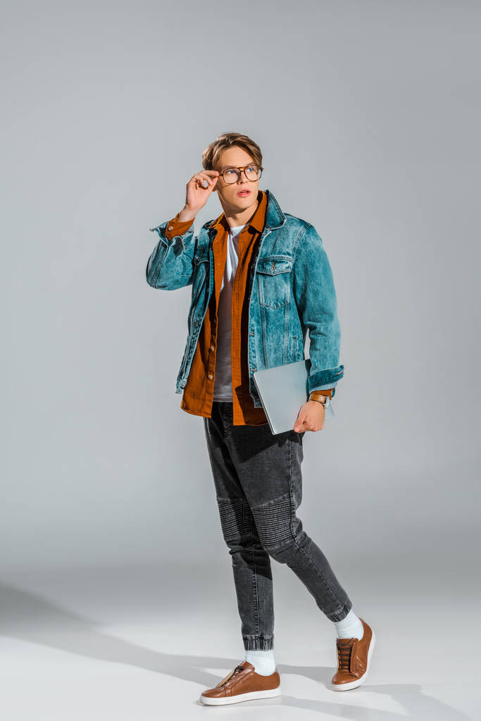 guapo elegante estudiante posando en chaqueta de mezclilla con portátil en gris
 - Foto, imagen