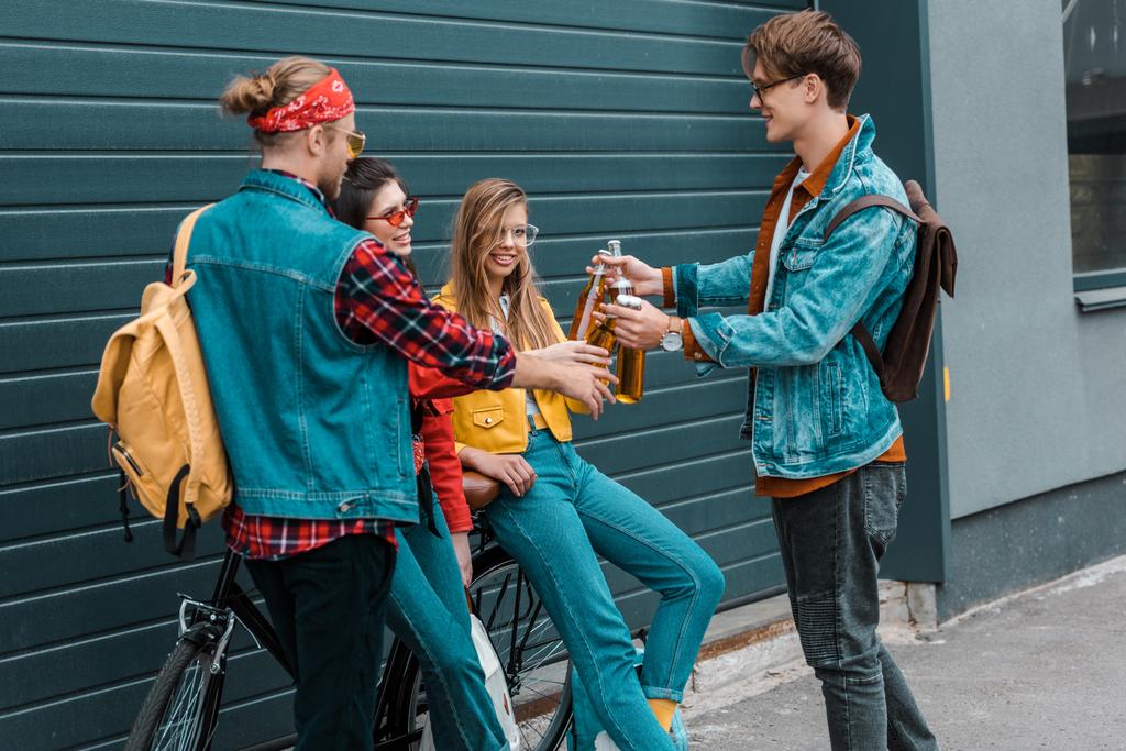 hipsters with bicycle clinking with beer bottles together on street - Photo, Image