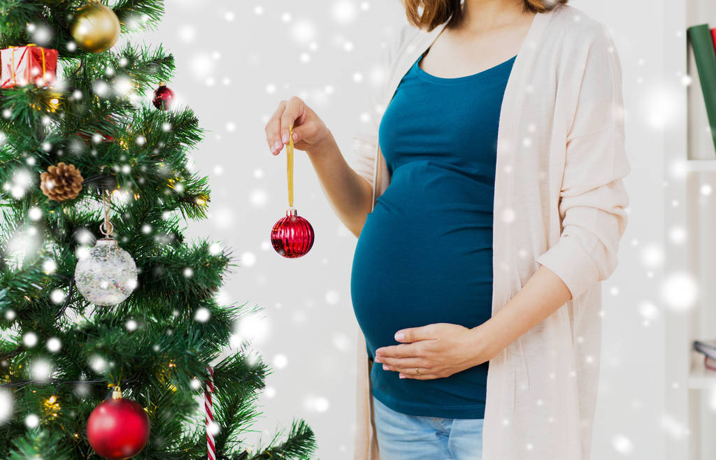 Mujer embarazada decorando árbol de Navidad
 - Foto, Imagen