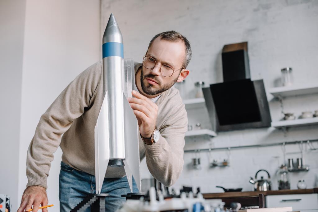 Ingeniero guapo modelando cohete y midiendo con regla en casa
 - Foto, imagen