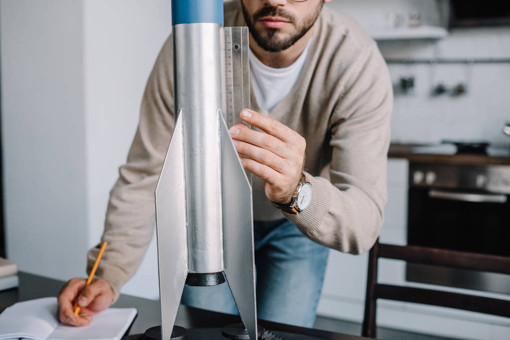 abgeschnittenes Bild eines Ingenieurs, der zu Hause Rakete modelliert und mit Lineal misst - Foto, Bild