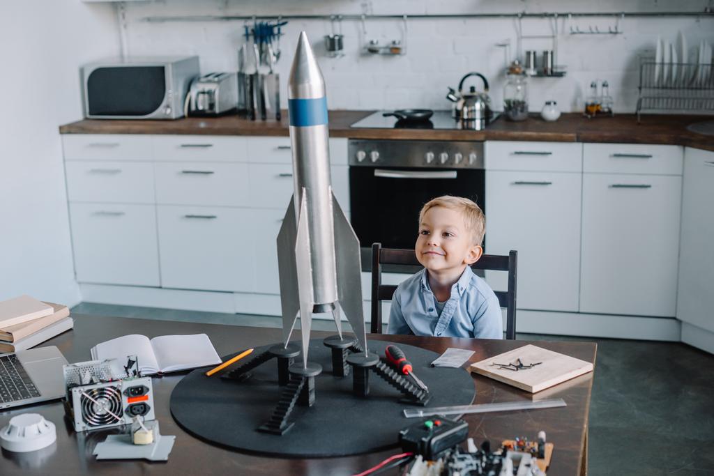 vidám imádnivaló fiú ül asztal rakéta modell konyhában a hétvégén - Fotó, kép