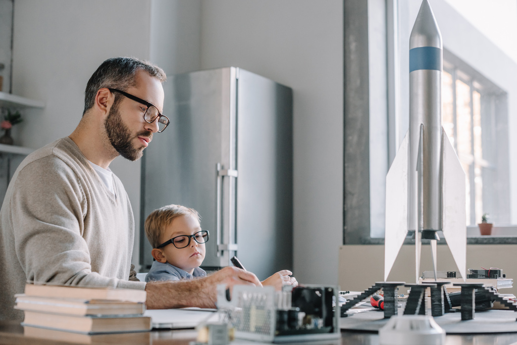 Vater und Sohn modellieren Rakete und schreiben zu Hause etwas am Tisch - Foto, Bild