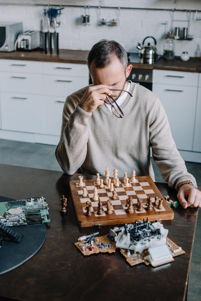 hoge hoekmening van moe man spelen schaak en aanraken van de neus brug thuis - Foto, afbeelding