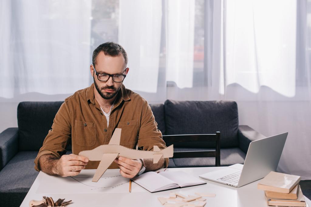 fokussierter Mann mit Brille und Pappflugzeug beim Modellieren zu Hause  - Foto, Bild