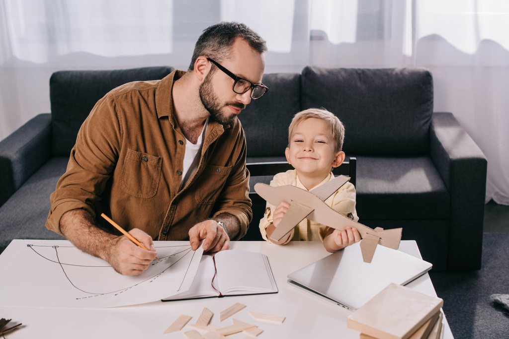 vader in brillen en schattig zoontje modelleren vliegtuig samen thuis - Foto, afbeelding