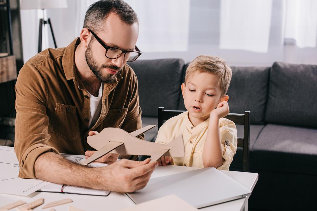father in eyeglasses and adorable little boy modeling wooden plane together - Photo, Image