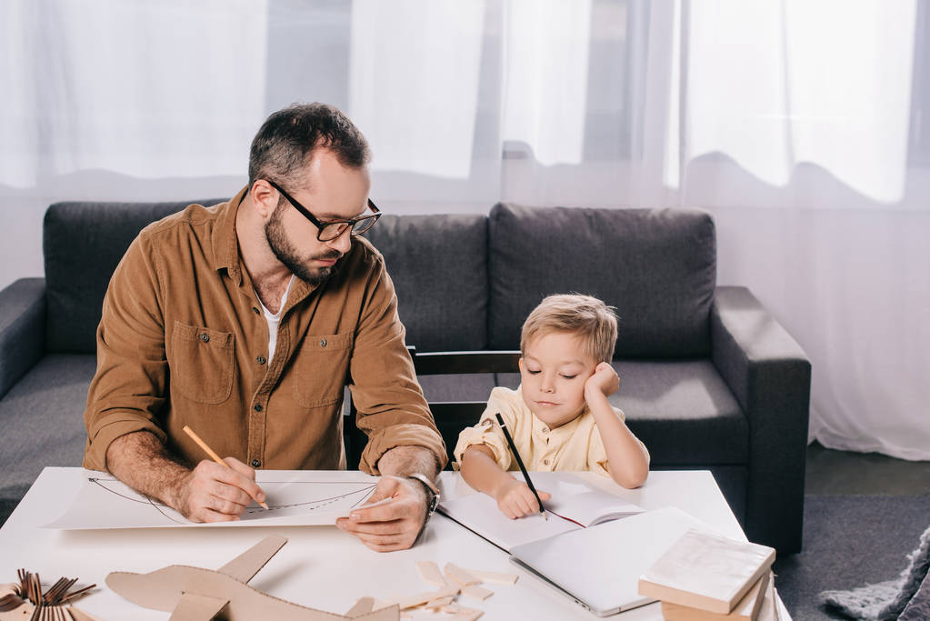 pai e pequeno filho desenho enquanto modelagem avião juntos em casa
  - Foto, Imagem